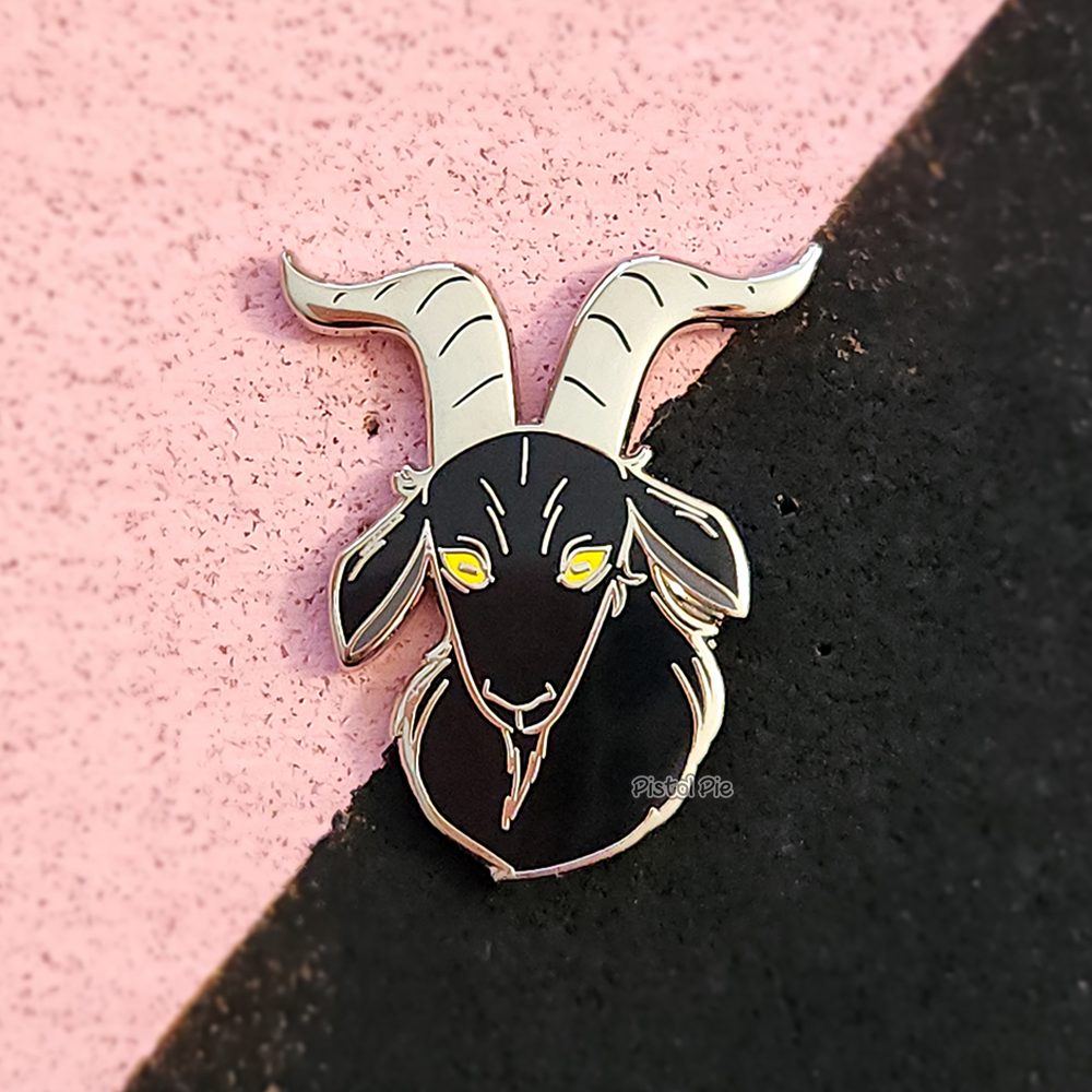 photo of a black goat enamel pin by pistol pie with yellow eyes and silver horns