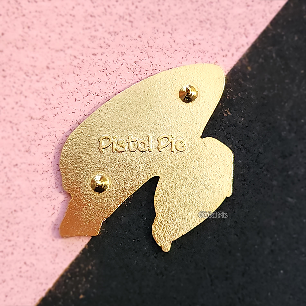 photo of the back of an enamel pin by pistol pie of a kawaii xenomorph alien school girl with toast in her mouth and Pistol Pie log embedded
