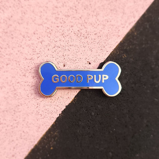 Blue bone-shaped pin with 'GOOD PUP' text on a pink and black background