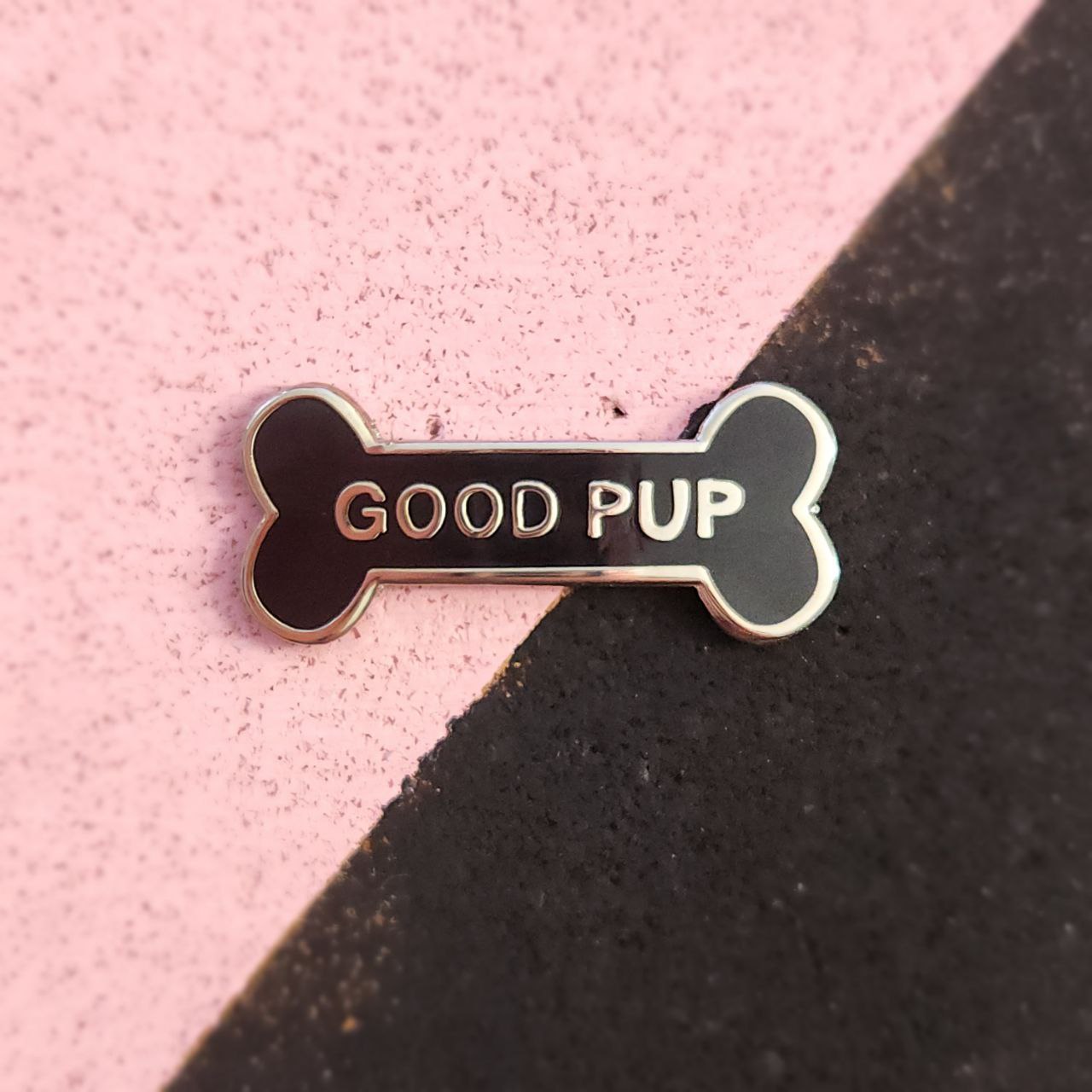 Bone-shaped pin with 'GOOD PUP' text on a pink and black background