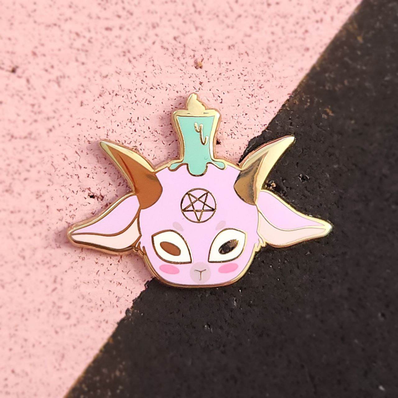 Enamel pin of a creature with horns on a pink and black background