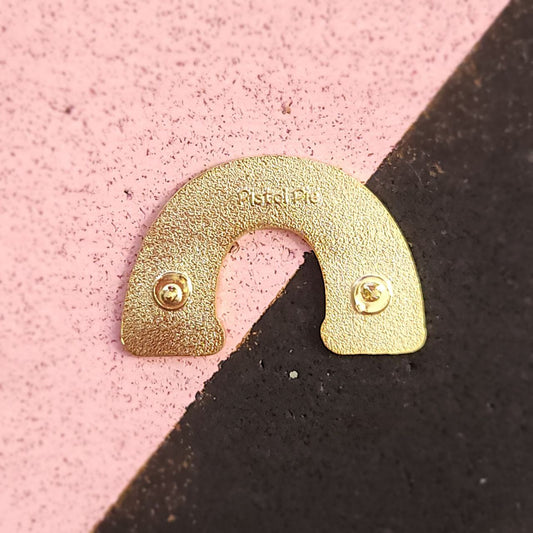 Gold arch-shaped pin on a pink and black background