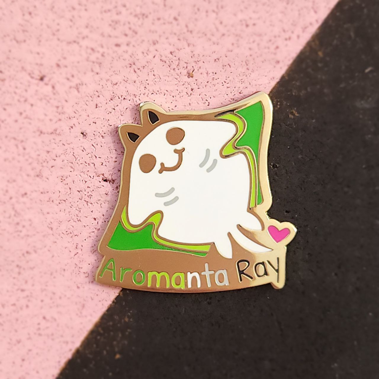Enamel pin of a cartoon character with 'Aromanta Ray' text on a pink and black background