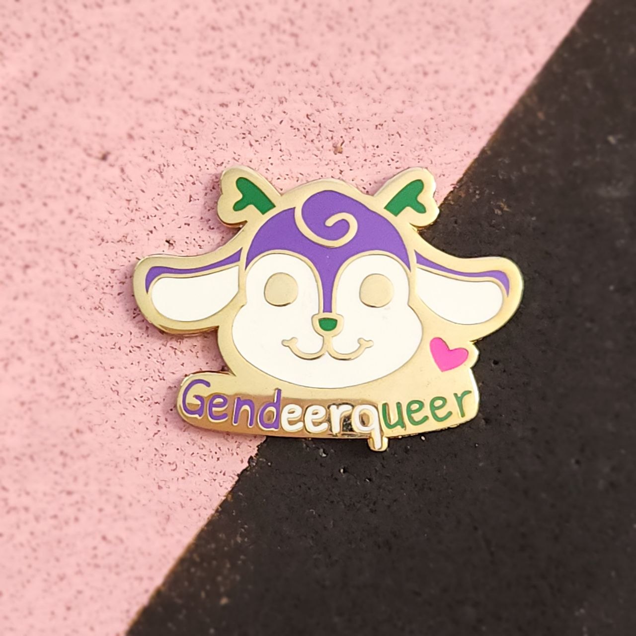 Enamel pin with a cartoon character and 'Gendeeroqueer' text on a pink and black background