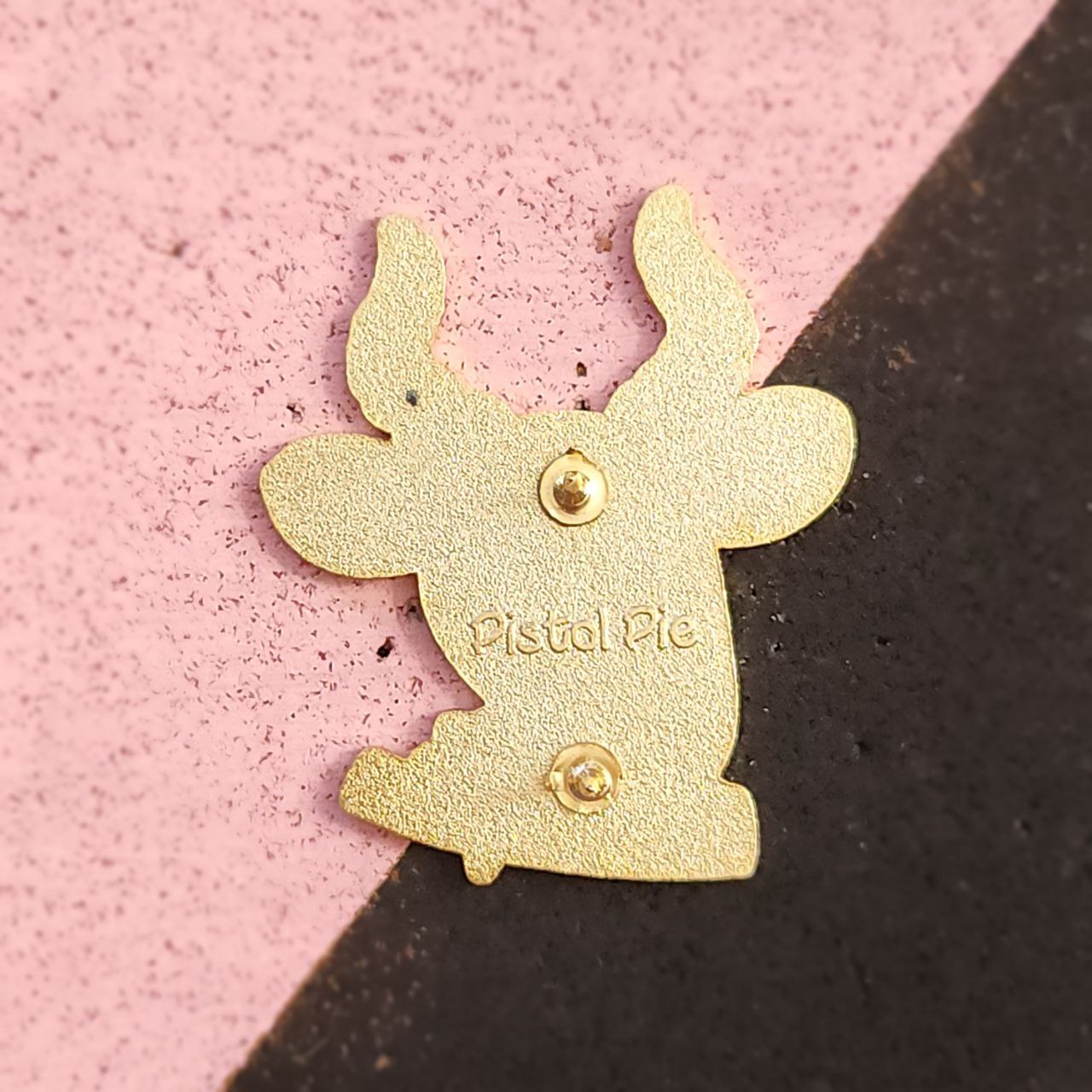 Gold object with 'Pistol Pie' branding on a pink and black background