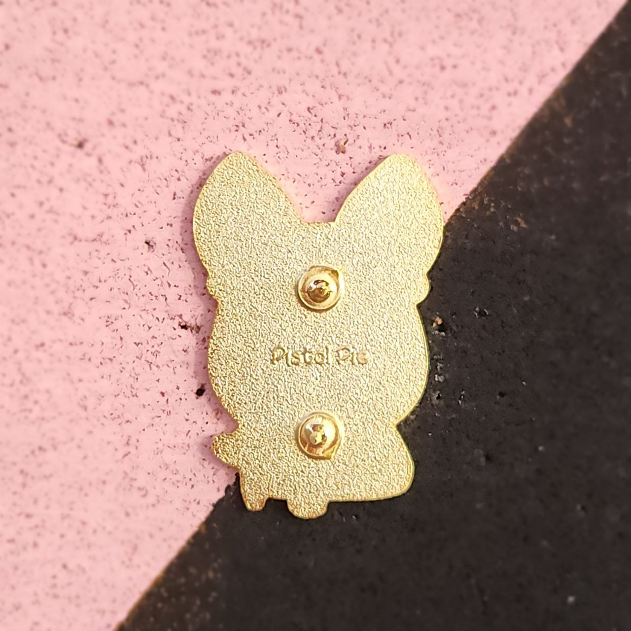 Gold dog-shaped pin a pink and black background