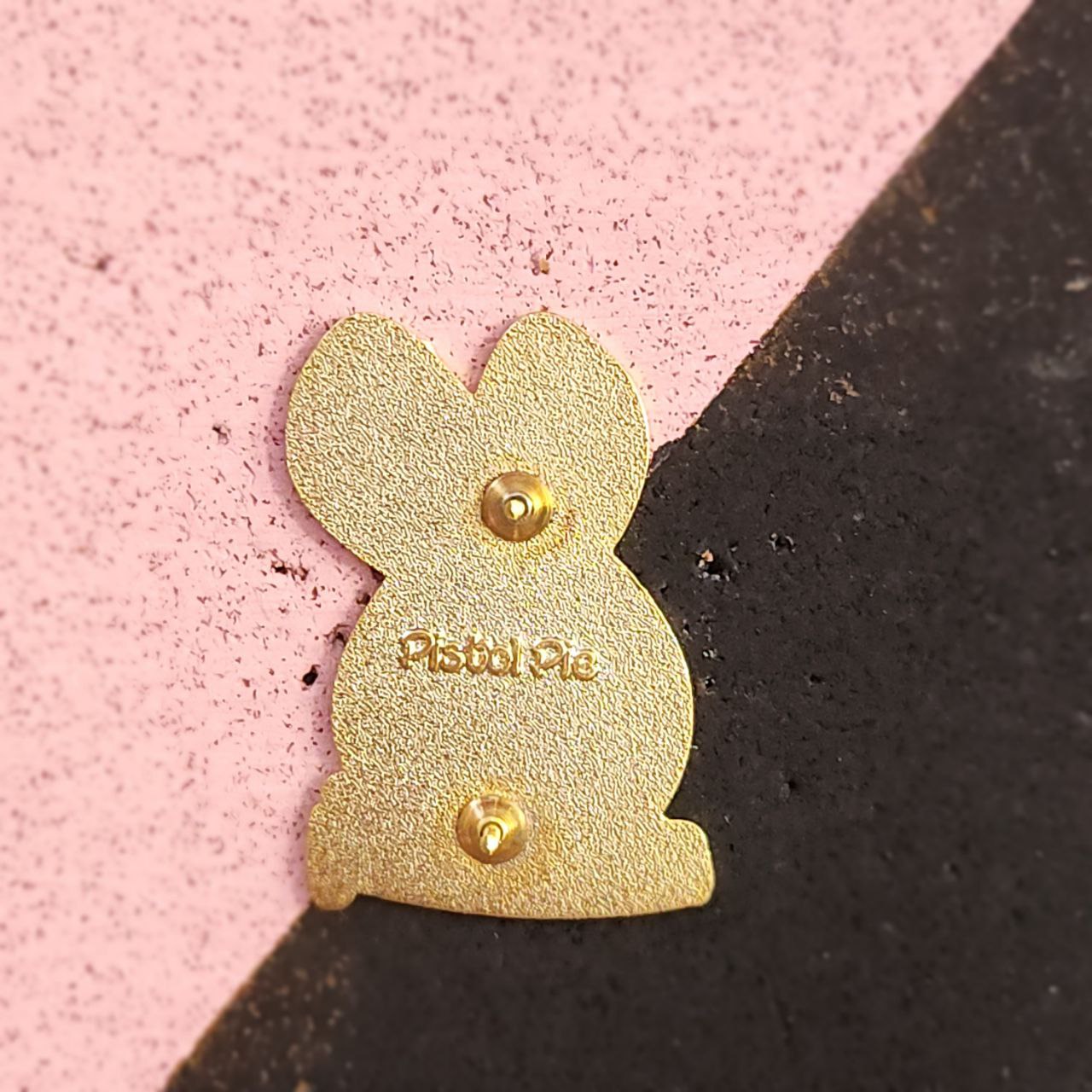 Gold bunny-shaped pinon a pink and black background