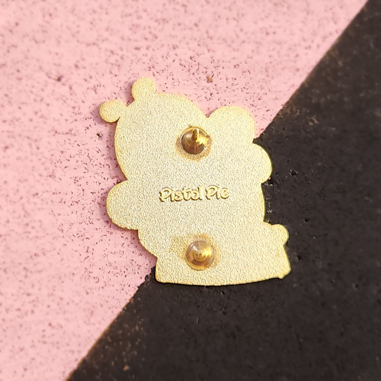 Gold-colored character-shaped pin with 'Pistil Pie' text on a pink and black background