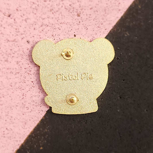 Gold-colored pin with 'Pistol Pie' branding on a pink and black background