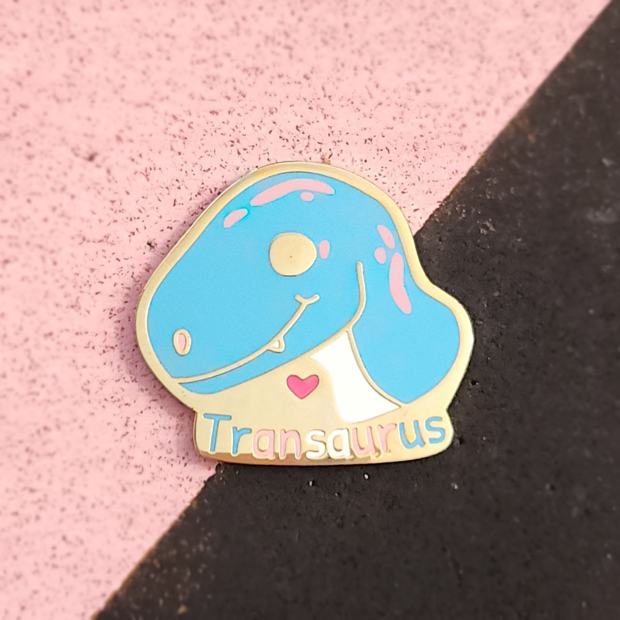 Pin with a blue dinosaur design labeled 'Transaurus' on a pink and black background